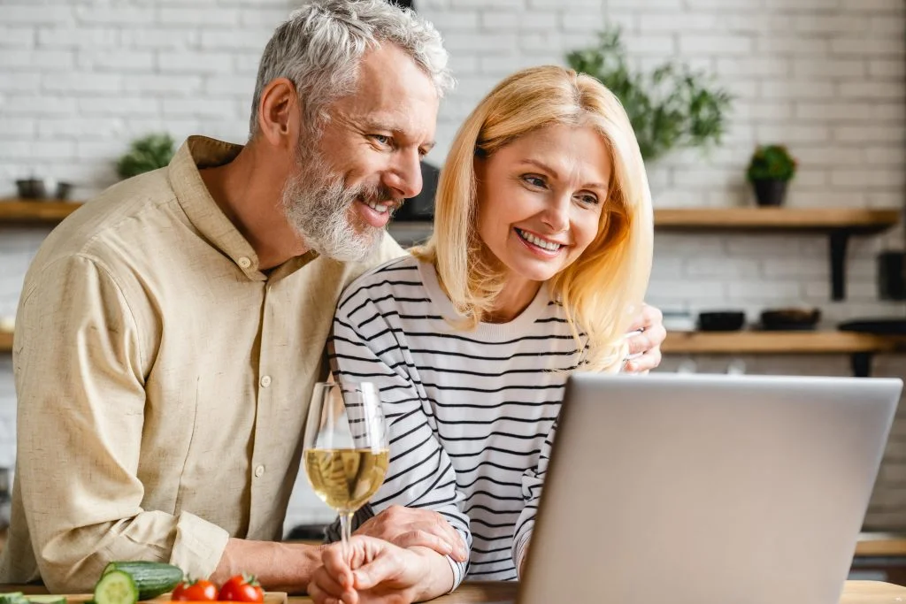 Middle aged couple watching in laptop and drinking wine