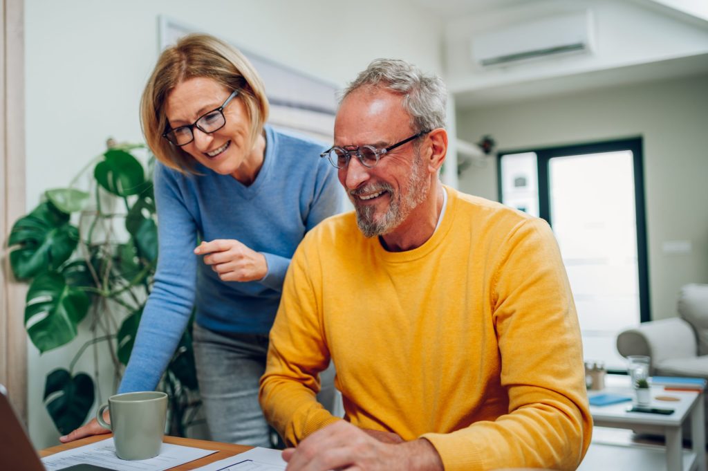 Senior middle aged happy couple using laptop together at home